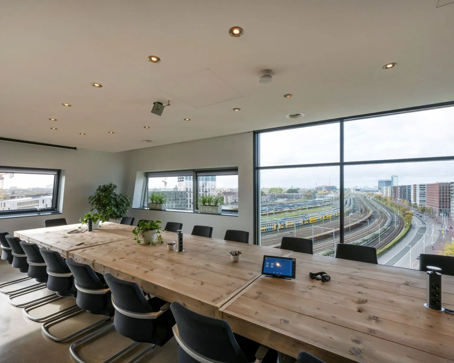 Vergaderzaal met lange houten tafel en uitzicht op spoorlijnen en gebouwen bij Rietlandpark in Amsterdam.