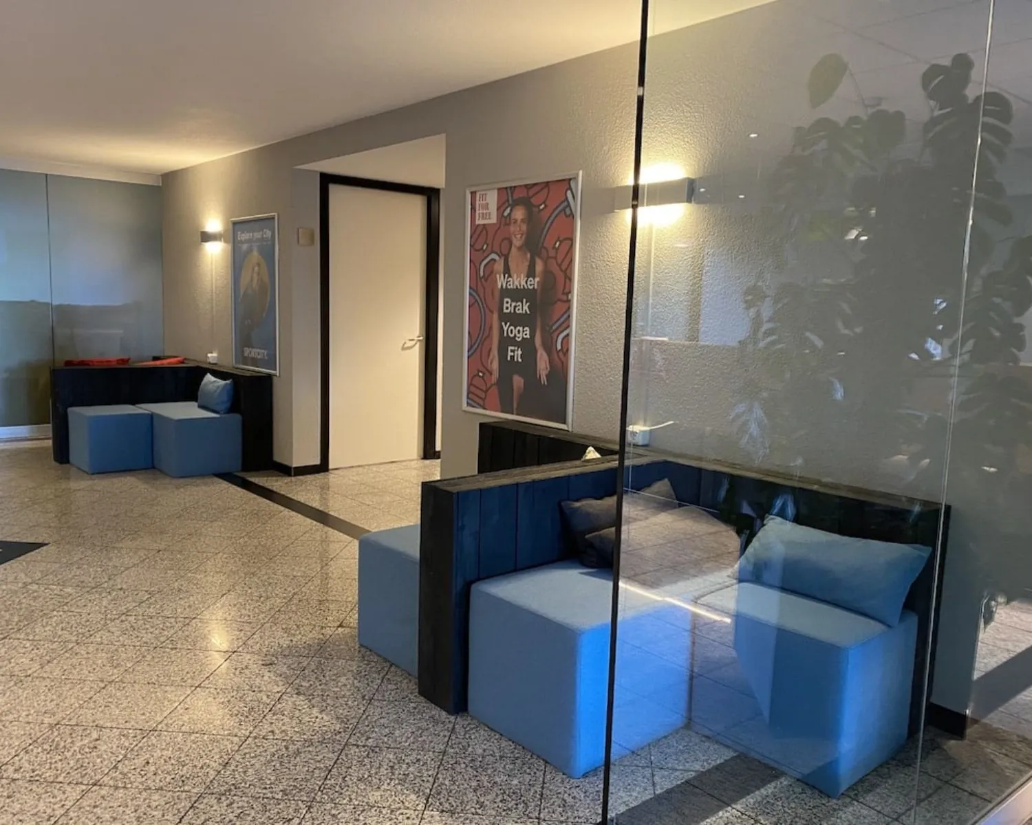 Moderne wachtruimte in kantoorruimte Elisabethhof in Leiderdorp met blauwe zitplekken en reclames aan de muur.