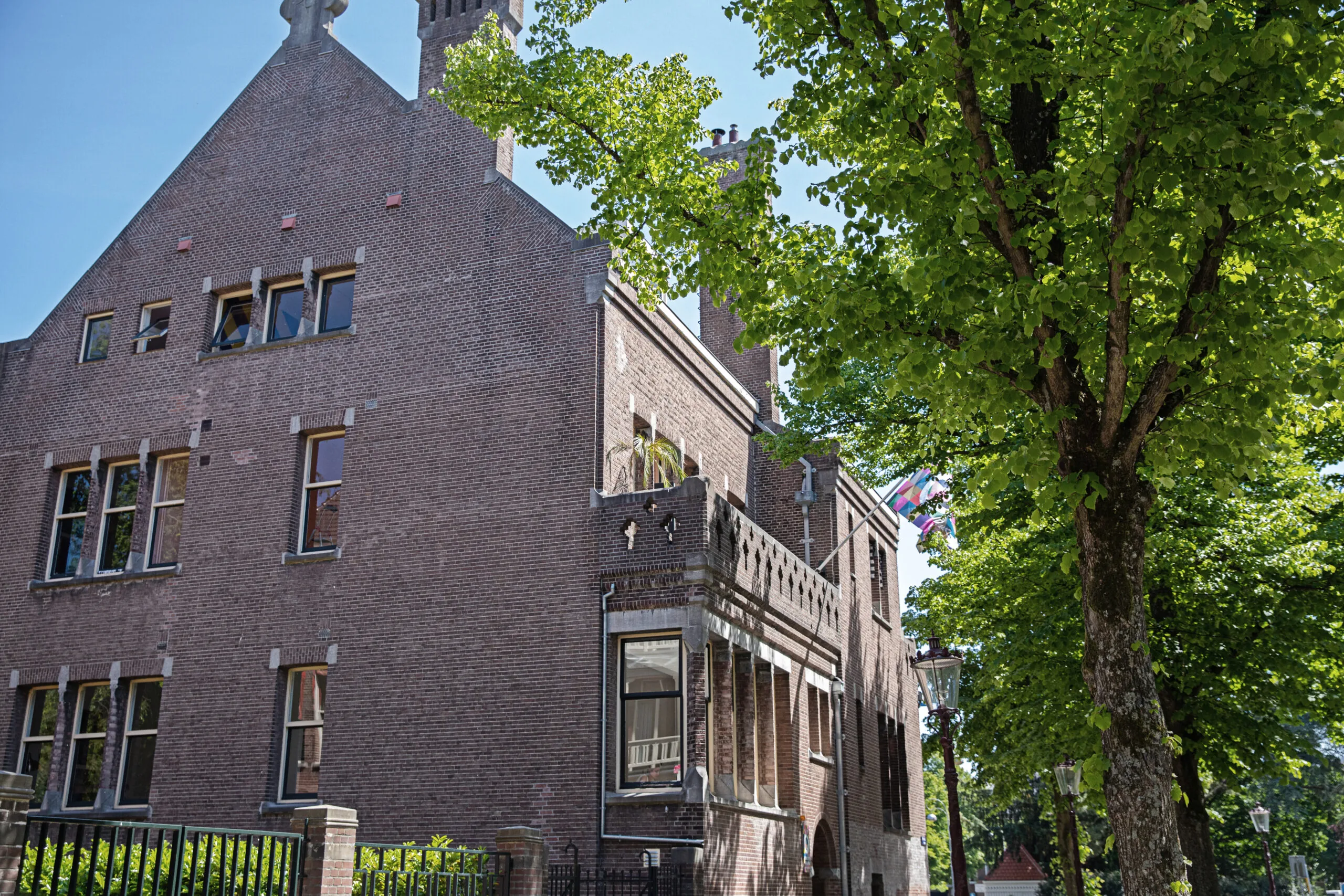 Bakstenen gebouw van Creativegrounds aan de Emmalaan, omgeven door bomen en vlaggen bij de ingang.