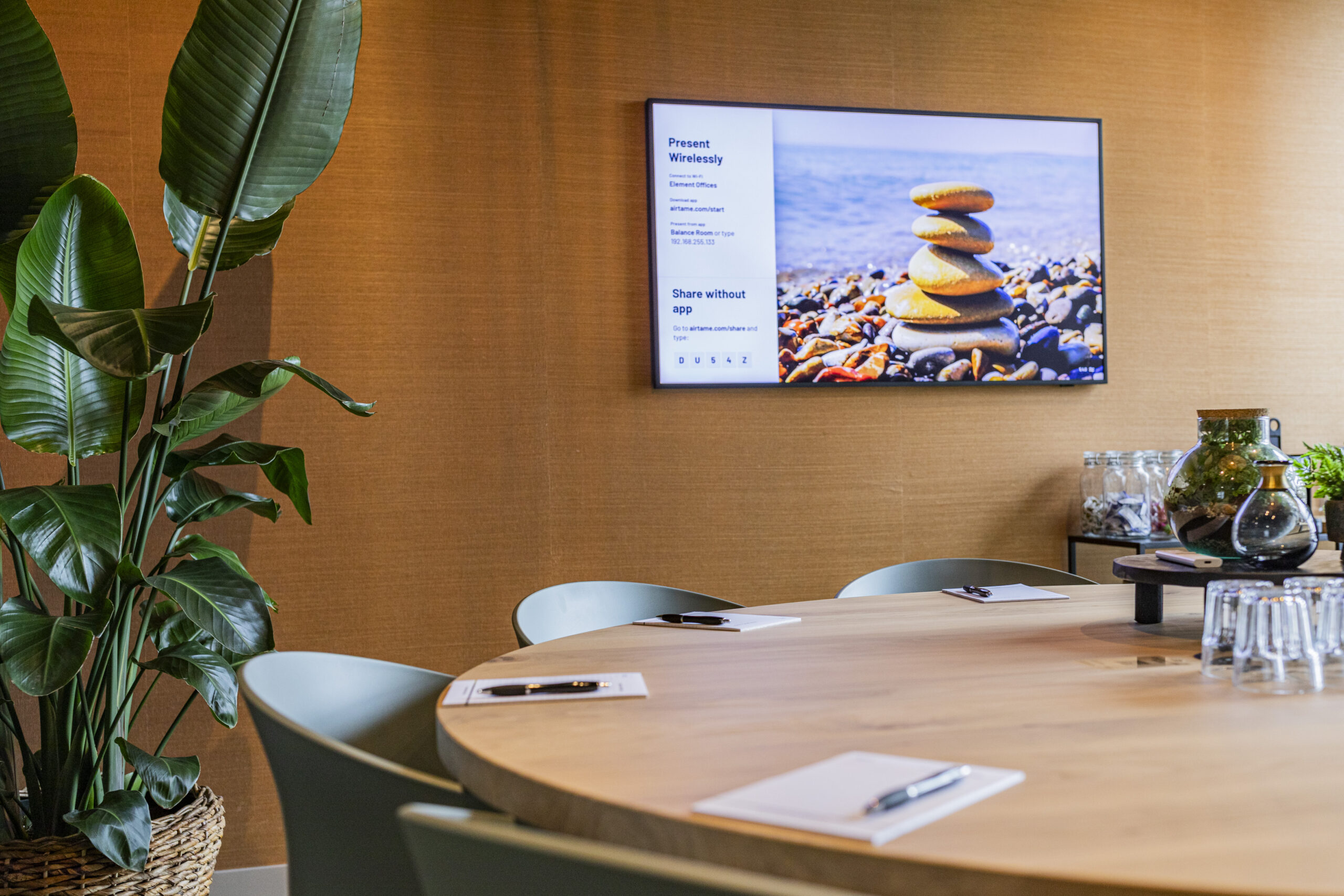 Een vergaderruimte in Rotterdam met een ronde houten tafel, grote plant en een beeldscherm dat rotsen toont.