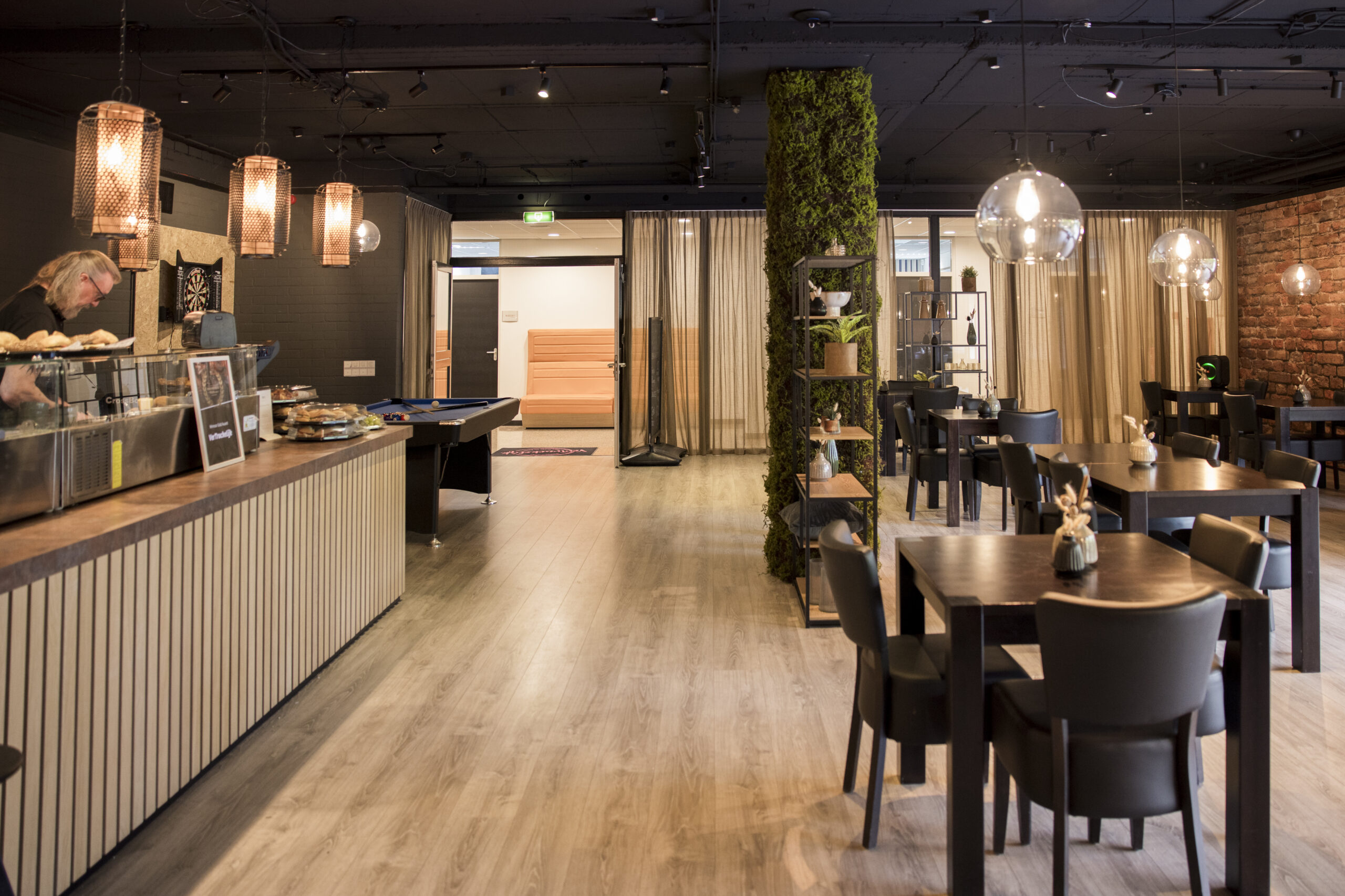 Een modern restaurantinterieur met houten tafels, een pooltafel, een bar en sfeervolle verlichting.