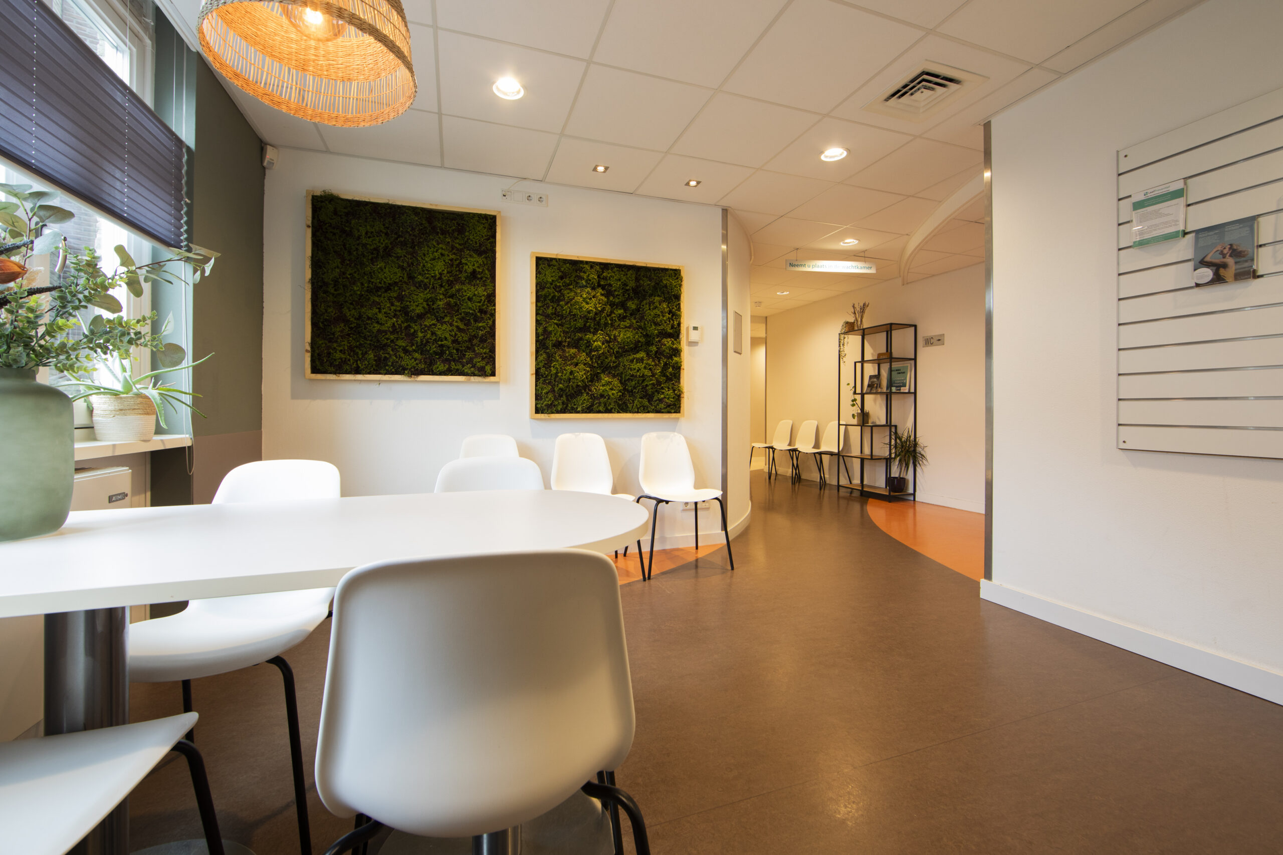 Een moderne wachtruimte met witte stoelen, een witte tafel, planten en groene muurdecoraties.