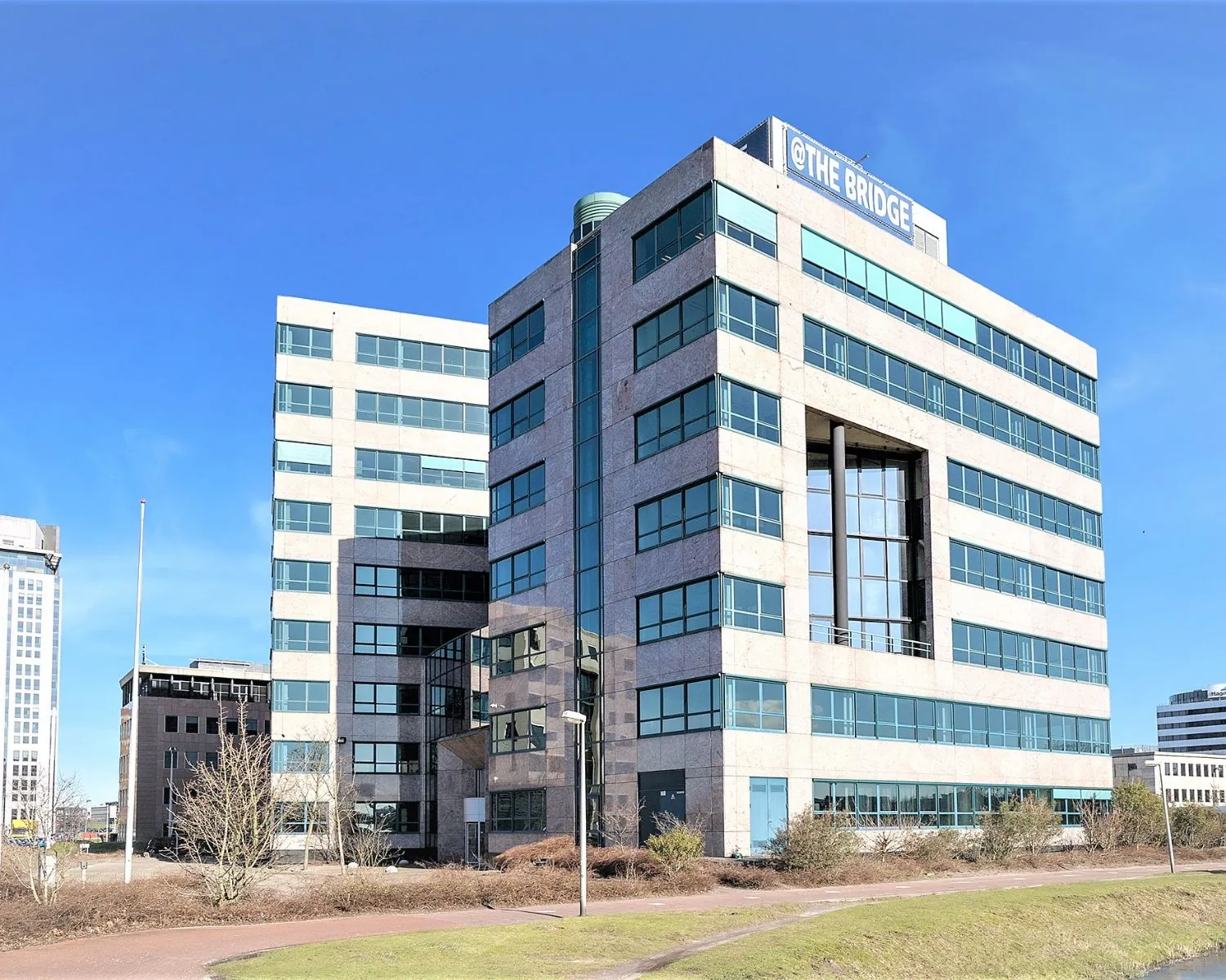 Zijaanzicht van modern kantoorgebouw @The Bridge met glazen gevel en meerdere verdiepingen.