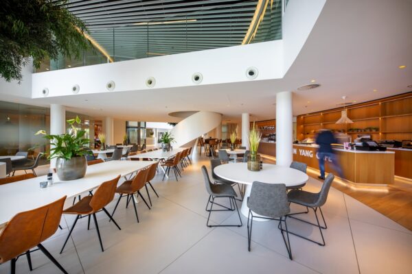 Moderne en ruim opgezette horecaruimte in kantoorpand aan de Euclideslaan, met zitplaatsen, groene planten en een koffiebar.