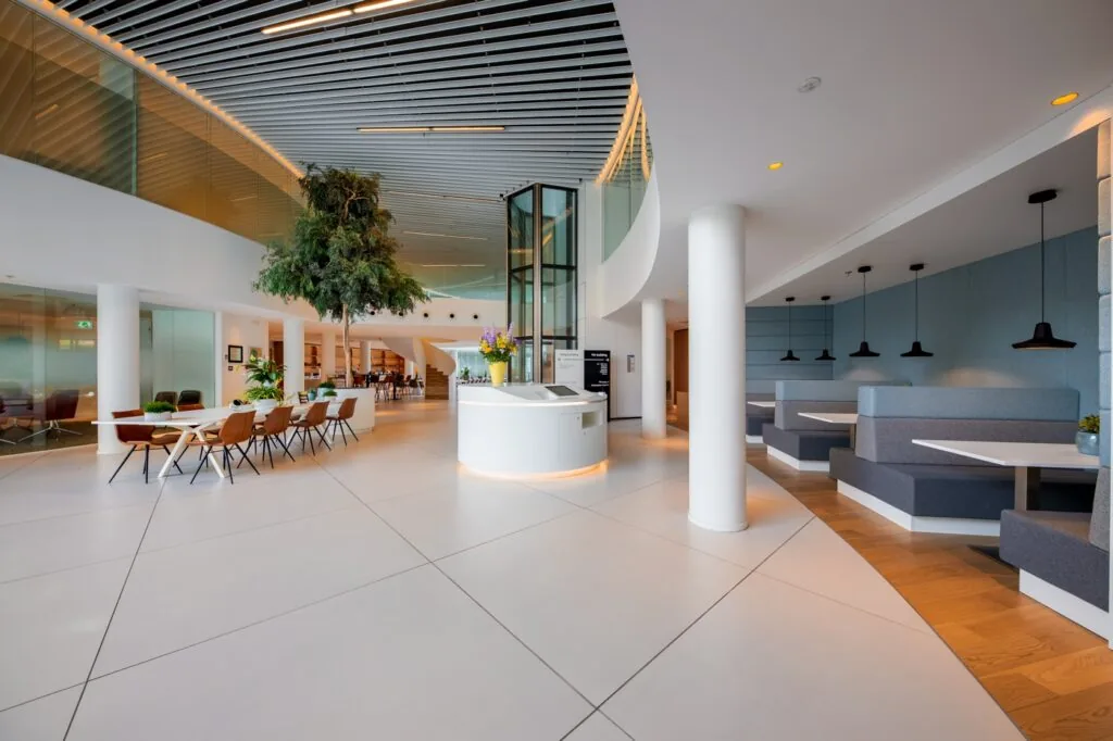 Moderne en ruimtelijke entreehal met zitgedeelte, receptiebalie en grote boom aan de Euclideslaan.