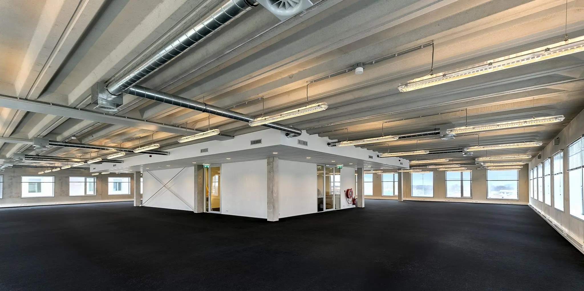 Ruim en licht kantoorpand aan de Bahialaan met hoog plafond, zichtbare leidingen en grote ramen.