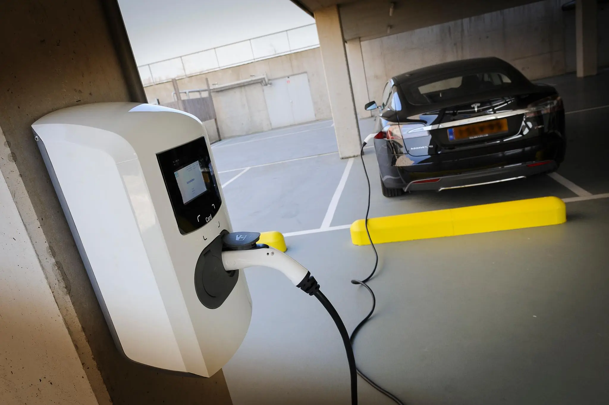 Een zwarte Tesla Model S wordt opgeladen bij een laadpaal in een overdekte parkeergarage aan de Bahialaan.