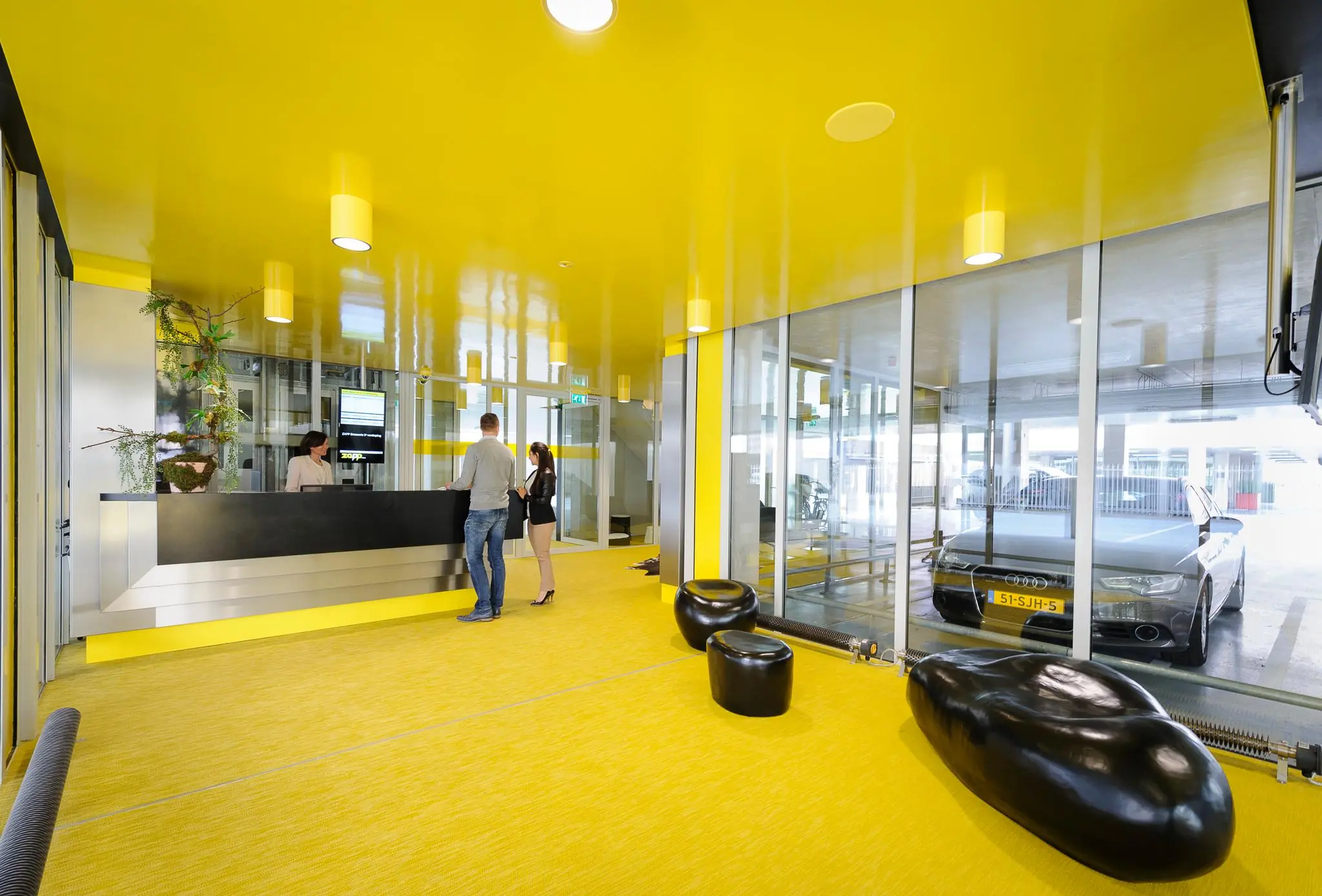 Moderne gele ontvangstruimte aan de Bahialaan met balie, wachtruimte en zicht op geparkeerde auto.
