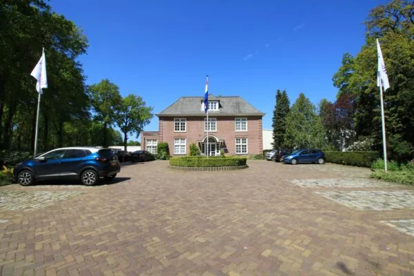 Vooraanzicht van een statig kantoorpand aan de Amersfoortsestraat met oprit, vlaggen en geparkeerde auto's.