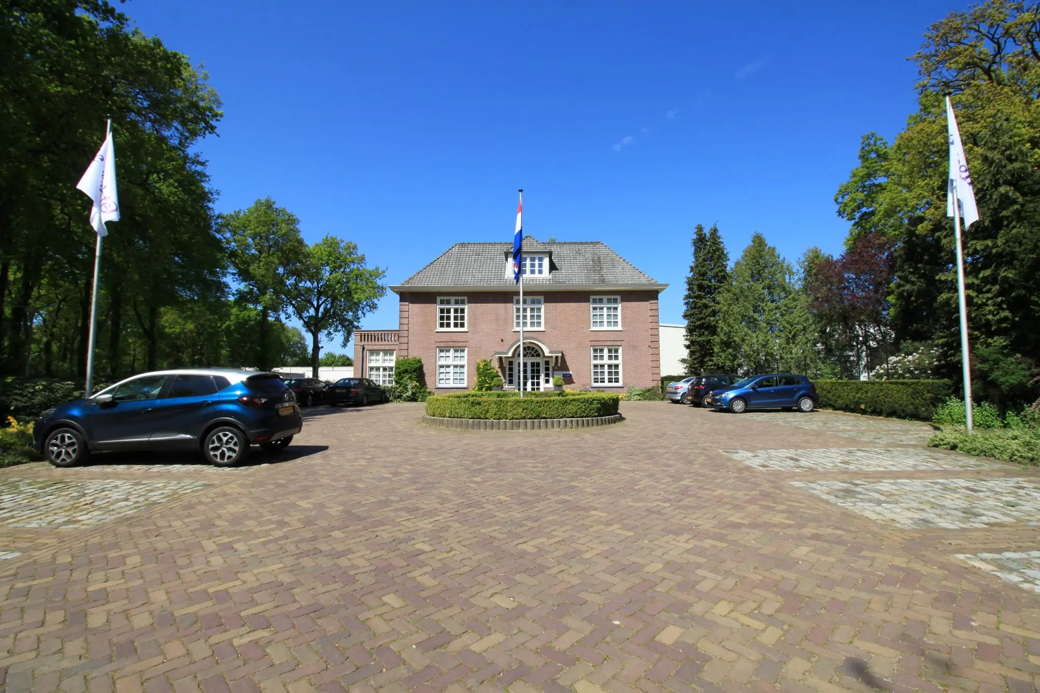 Vooraanzicht van een statig kantoorpand aan de Amersfoortsestraat met oprit, vlaggen en geparkeerde auto's.