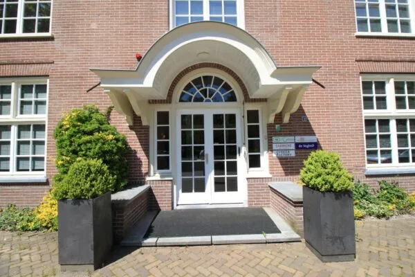 Ingang van een bakstenen kantoorpand aan de Amersfoortsestraat met witte dubbele deuren, decoratieve overkapping en borden met bedrijfsnamen.
