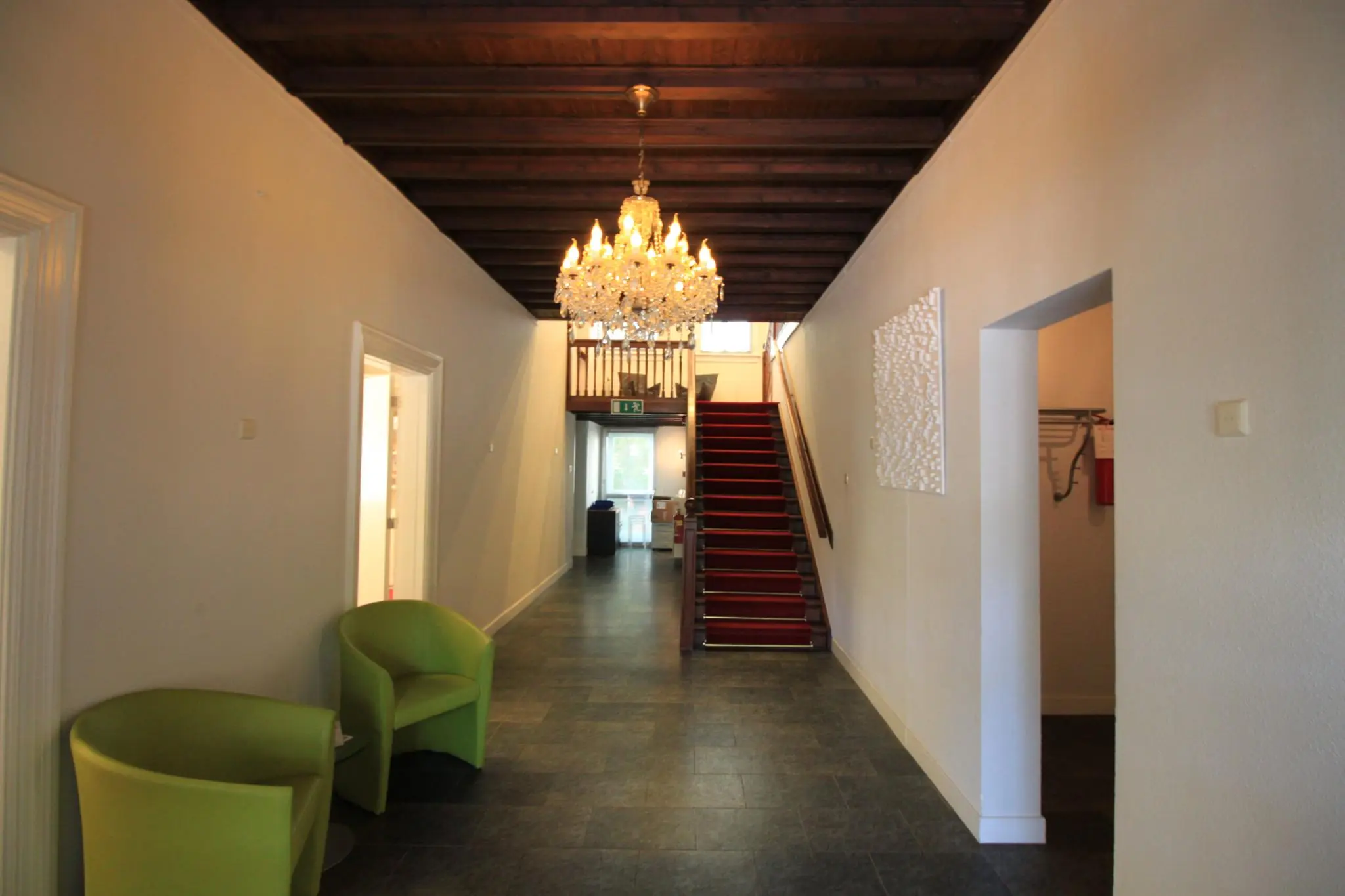 Hal met een houten plafond, kristallen kroonluchter, rode traploper en twee groene stoelen in een pand aan de Amersfoortsestraat.