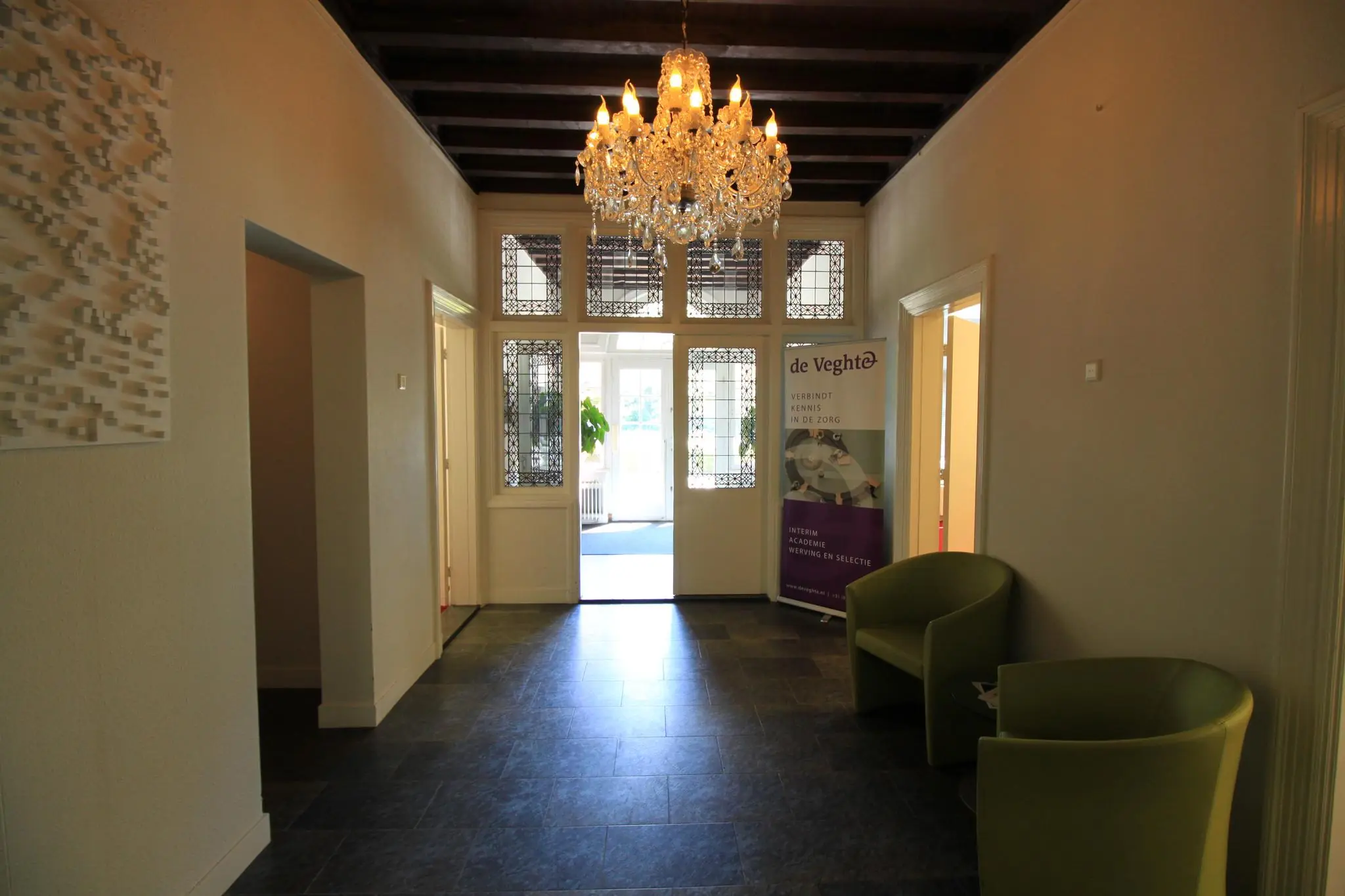 Hal met klassieke uitstraling in een pand aan de Amersfoortsestraat, met kroonluchter, glas-in-loodramen en een banner van zorgorganisatie De Veght.