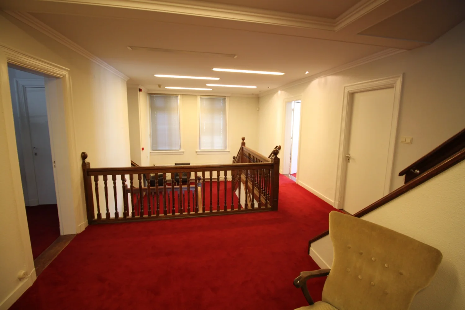 Hal met rode vloerbedekking, houten trapleuning en meerdere deuren in een pand aan de Amersfoortsestraat.