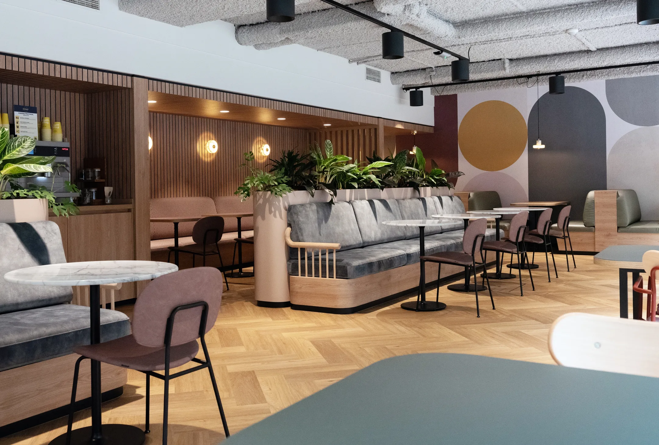 Een moderne, minimalistische gemeenschappelijke ruimte met tafels, stoelen en veel planten.