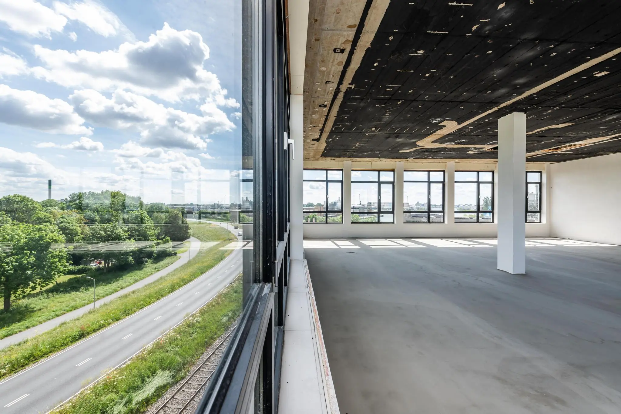 Licht en leeg industrieel interieur met grote ramen en uitzicht op de Lindtsedijk en het omliggende groen.
