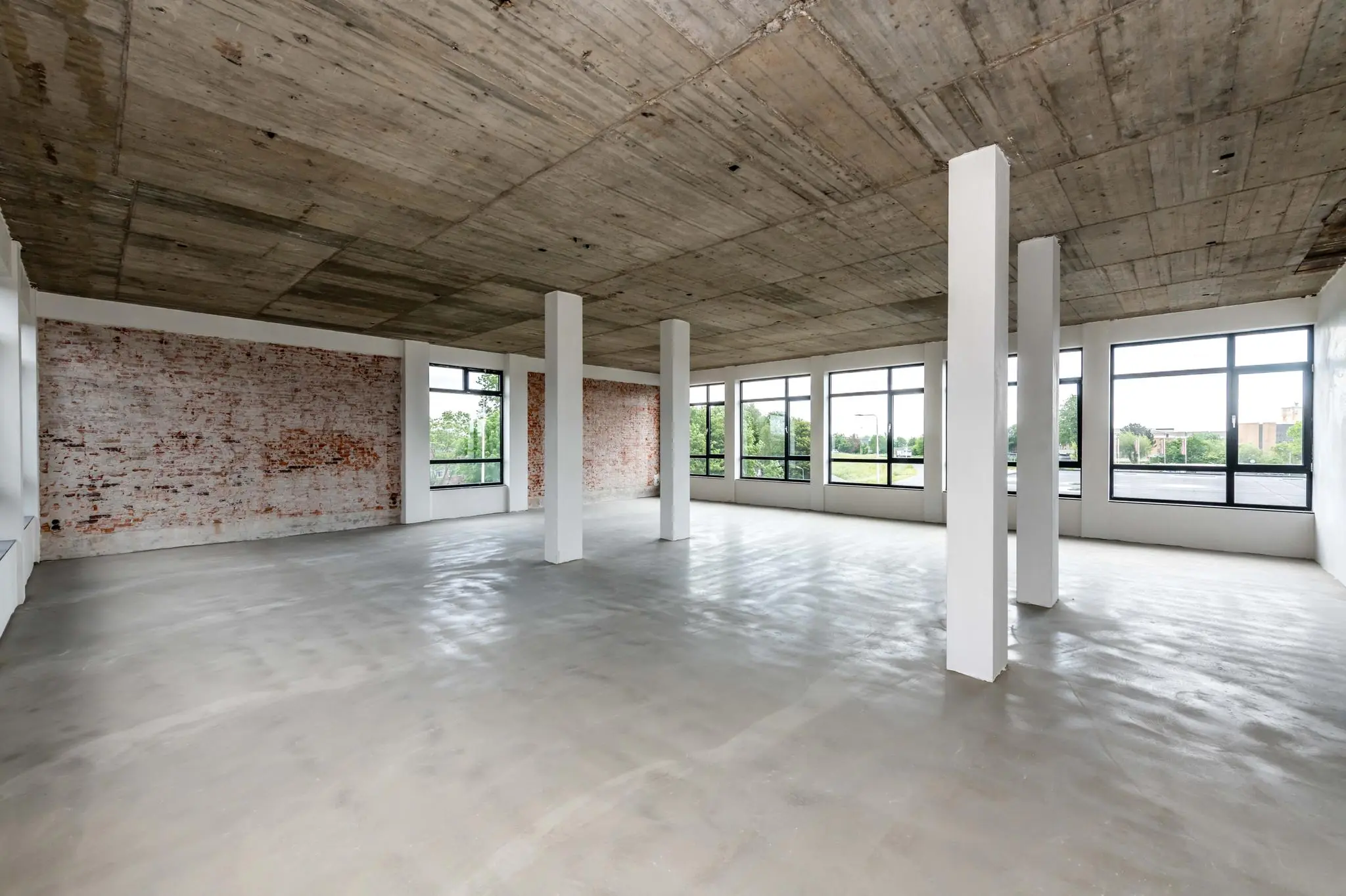 Een lege, industriële ruimte met betonnen plafond, bakstenen muur en grote ramen aan de Lindtsedijk.