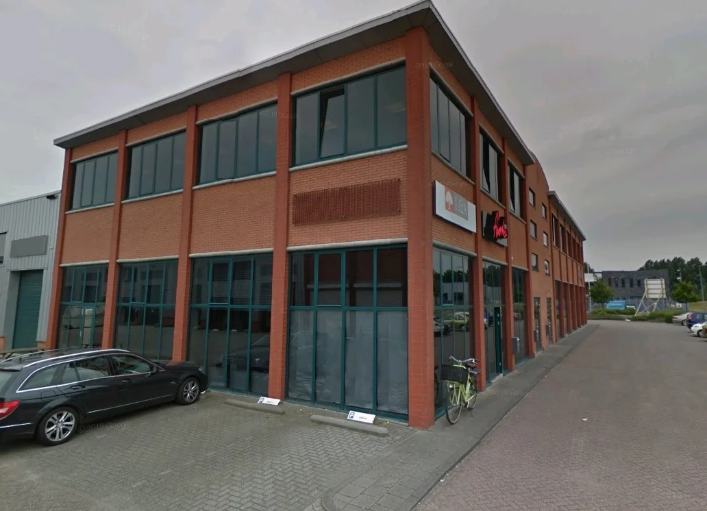 Bakstenen kantoorpand op de Sydneystraat met grote ramen, geparkeerde auto's en fietsen voor de ingang.