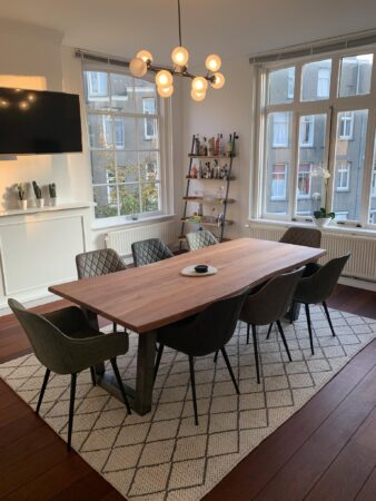 Moderne eethoek aan de Keizersgracht met houten tafel, zes stoelen, designlamp en uitzicht op Amsterdamse gevels.