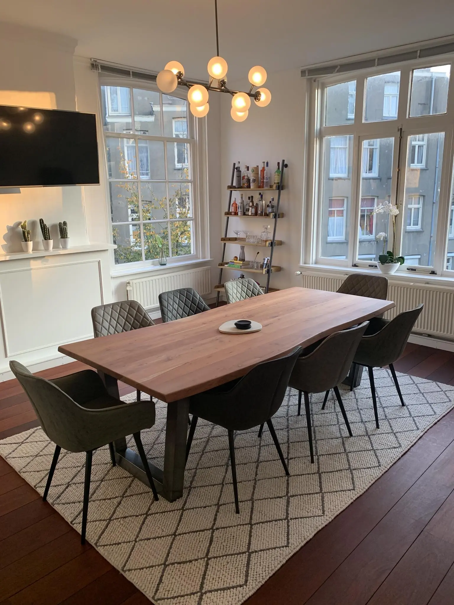 Moderne eethoek aan de Keizersgracht met houten tafel, zes stoelen, designlamp en uitzicht op Amsterdamse gevels.