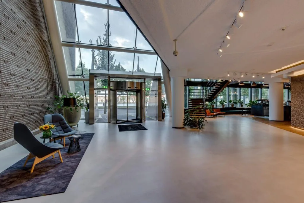 Moderne en lichte entreehal van een kantoorpand aan de Boompjes met glazen gevel, zitgedeelte en trap naar de bovenverdieping.