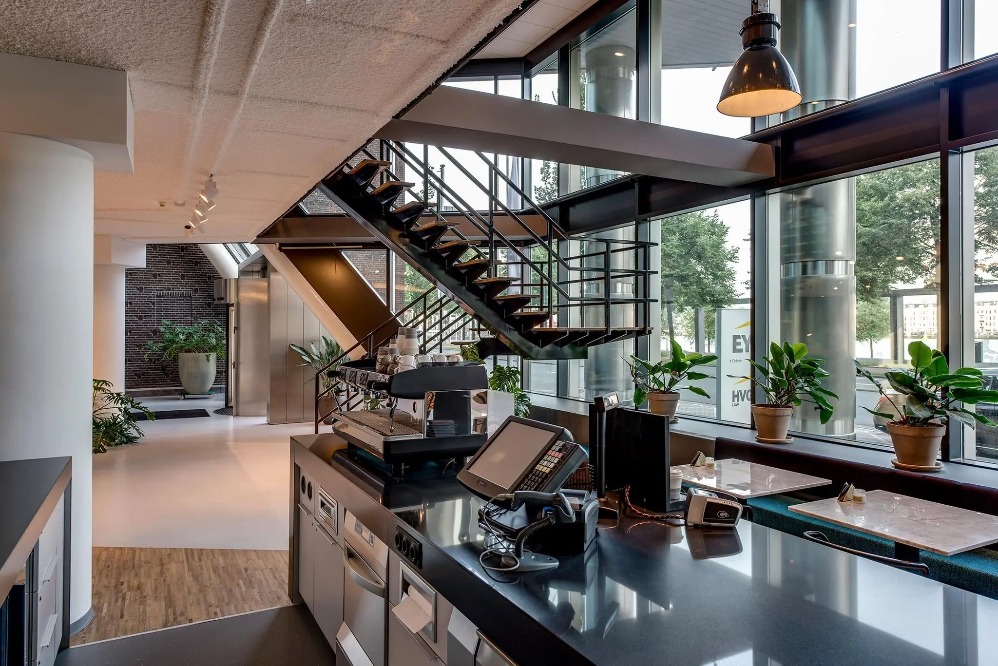 Modern interieur van een horecagelegenheid aan de Boompjes met grote ramen, een open trap en een strak ingericht barista-gedeelte.