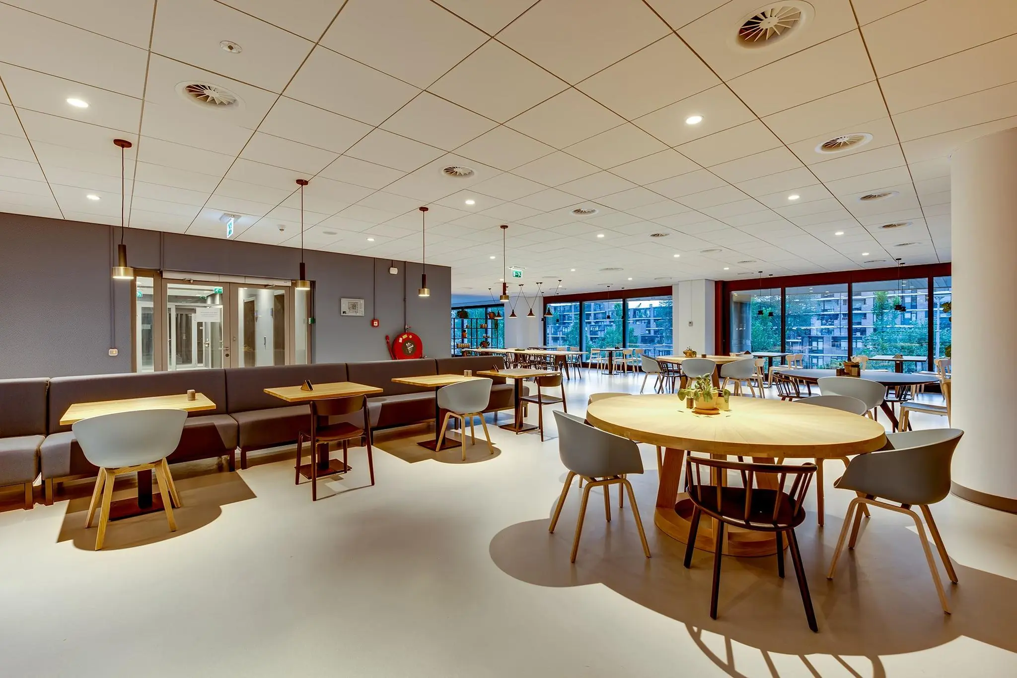 Moderne en lichte bedrijfskantine in Boompjes met houten tafels, designstoelen en grote ramen met uitzicht op de stad.
