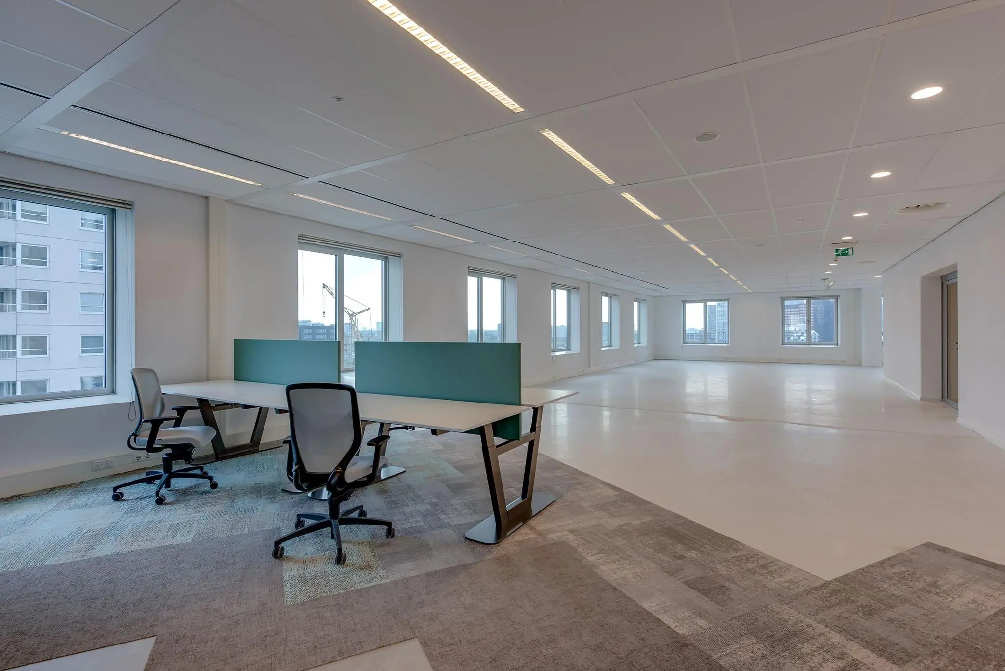 Moderne, lichte kantoorruimte in het Boompjes-gebouw met bureaus, stoelen en uitzicht op de stad.