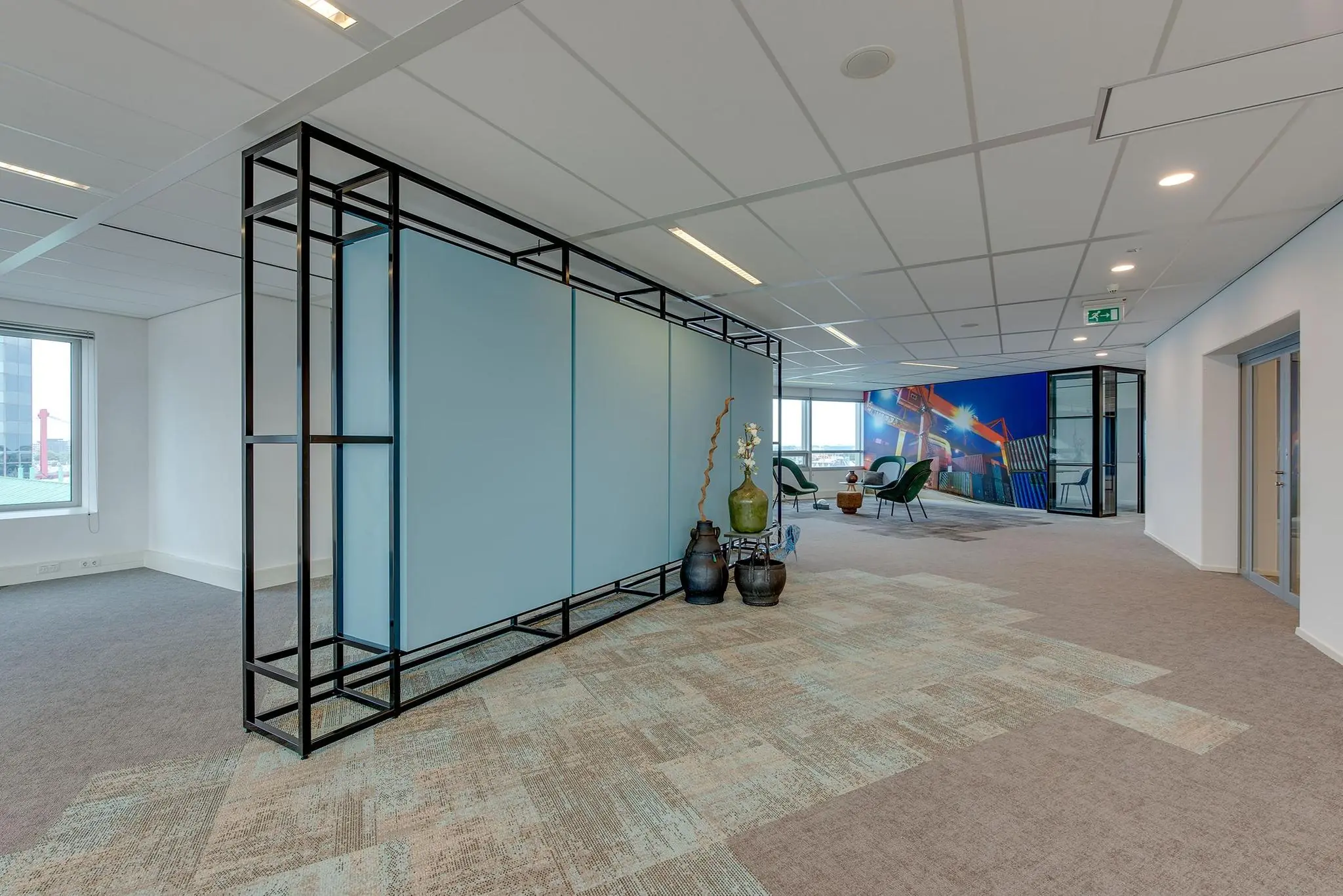Modern kantoorinterieur met een glazen scheidingswand, decoratieve vazen en een zitgedeelte met uitzicht op een muurschildering van havencontainers.