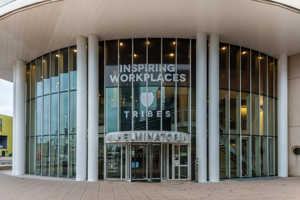 Entree van de Wilhelminatoren met glazen gevel en opschrift "Inspiring Workplaces – Tribes".