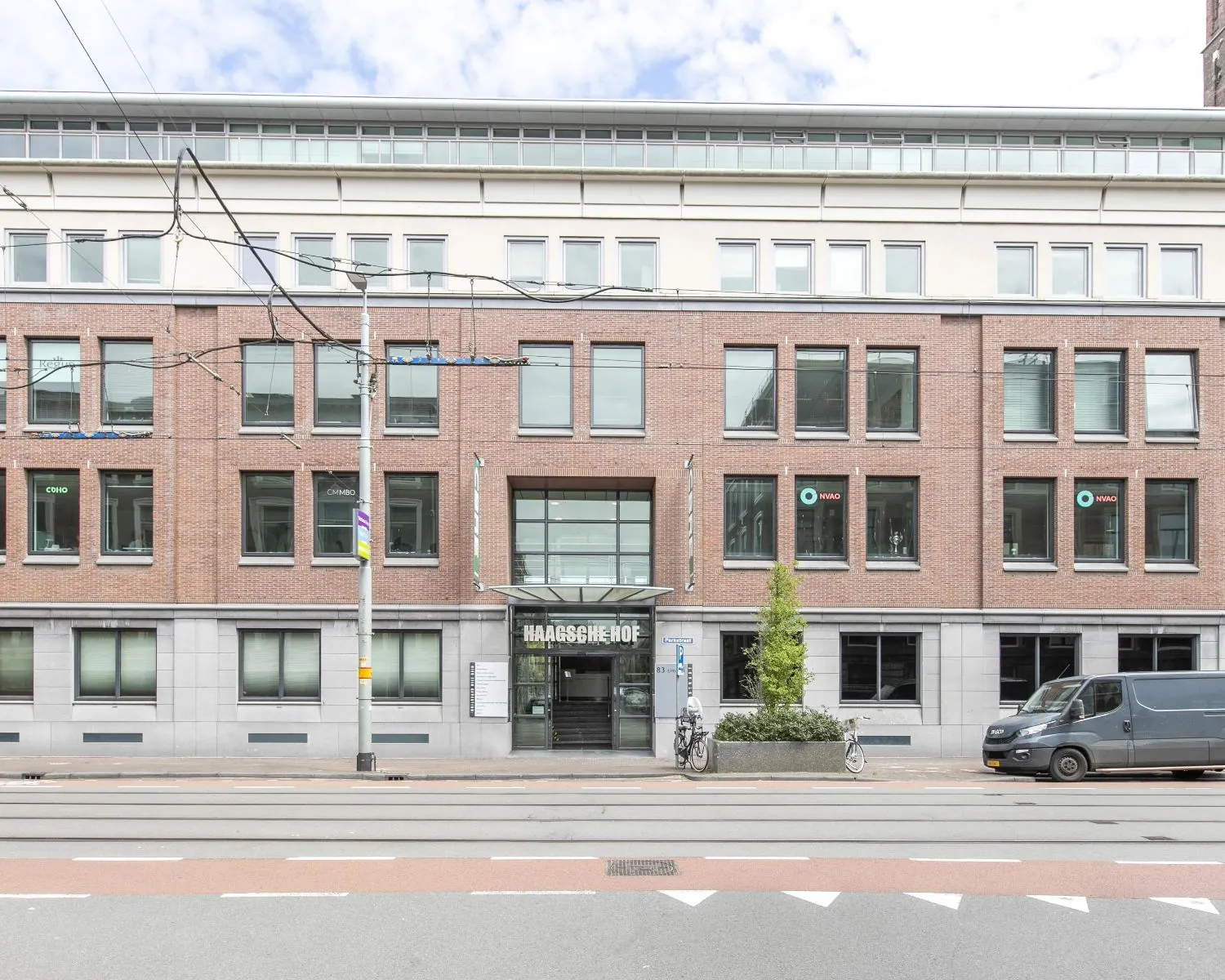 Voorgevel van het kantoorgebouw 'Haagse Hof' aan een trambaan met geparkeerde fietsen en busje.