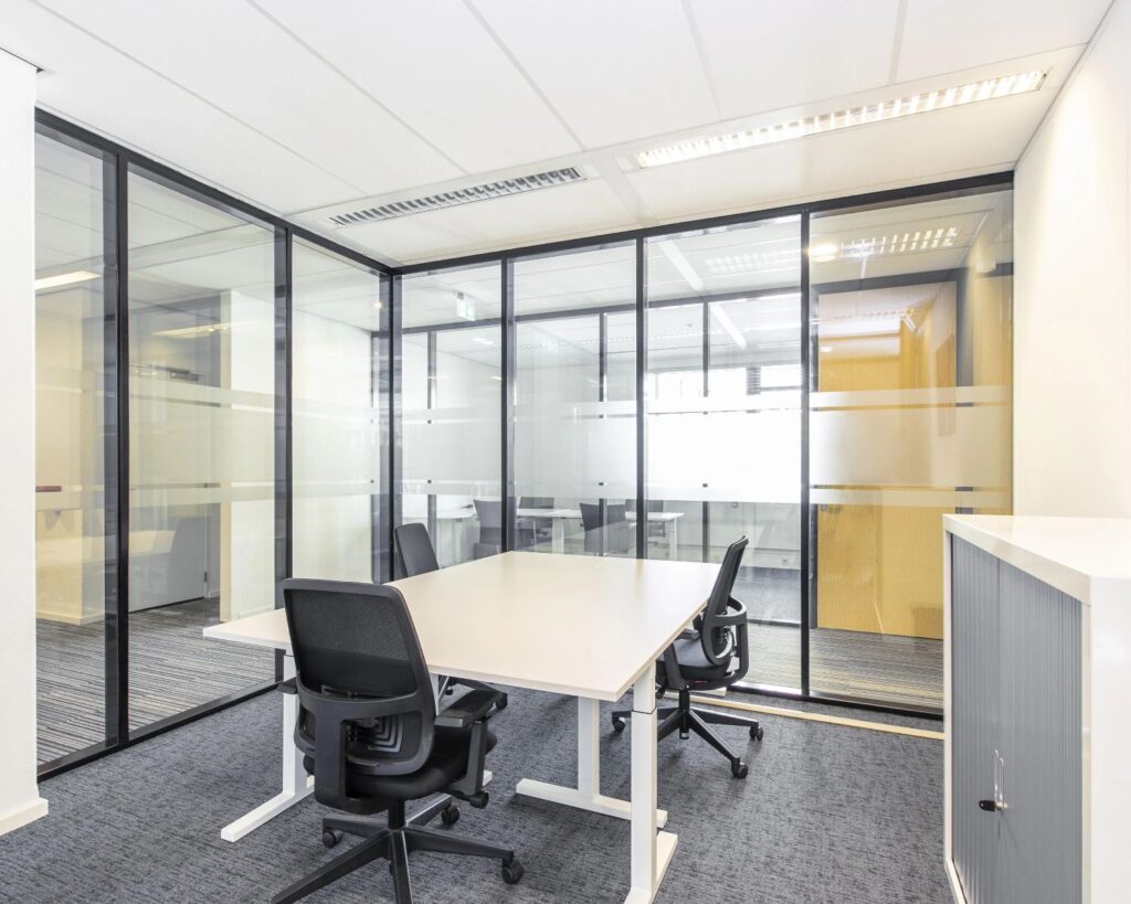 Moderne, lichte vergaderruimte met glazen wanden, een witte tafel en vier zwarte bureaustoelen.