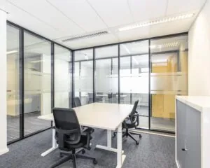 Moderne, lichte vergaderruimte met glazen wanden, een witte tafel en vier zwarte bureaustoelen.