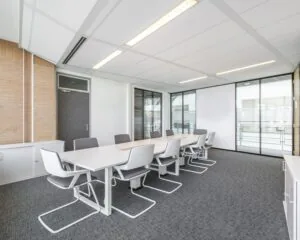 Moderne vergaderruimte met een lange witte tafel, grijze stoelen en glazen wanden.