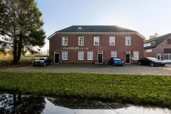 Vooraanzicht van het kantoorpand van J. v.d. Veldt & Zn BV aan de Sloterweg met geparkeerde auto's en een sloot op de voorgrond.