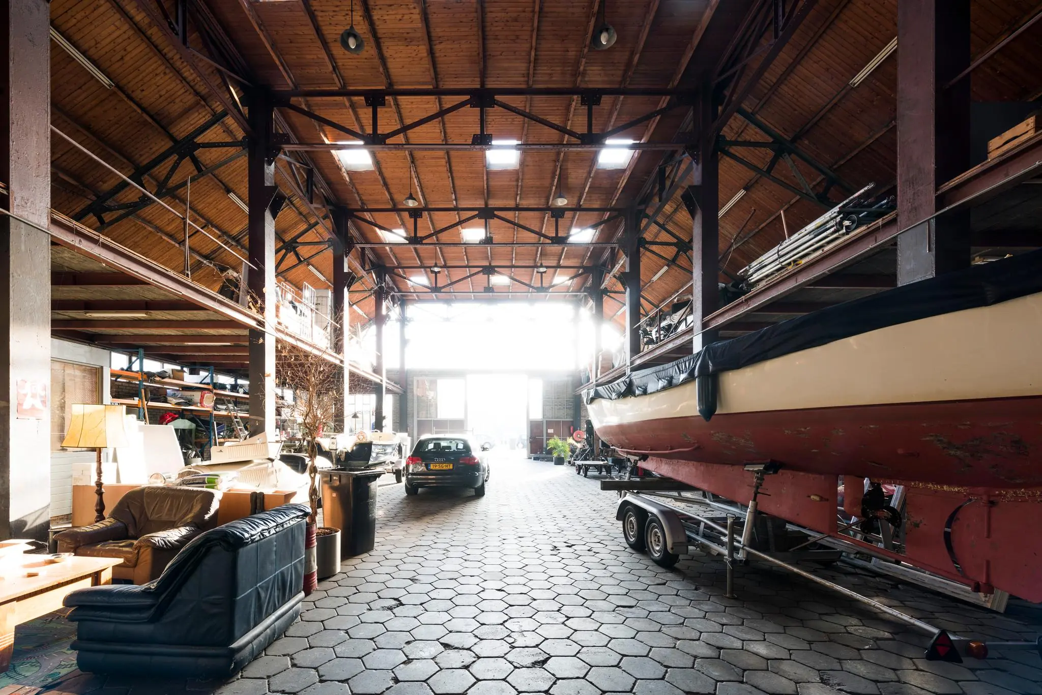 Interieur van een ruime loods aan de Sloterweg met een boot op een trailer, geparkeerde auto en diverse opslagmaterialen.