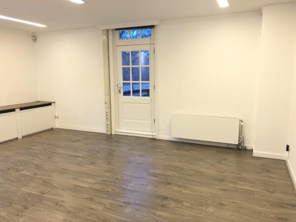 Licht en leeg vertrek met houten vloer, witte muren en een deur naar buiten aan de Amersfoortsestraat.