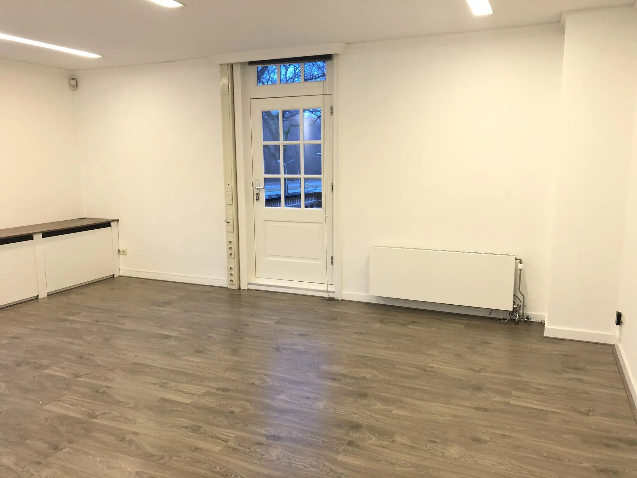 Licht en leeg vertrek met houten vloer, witte muren en een deur naar buiten aan de Amersfoortsestraat.