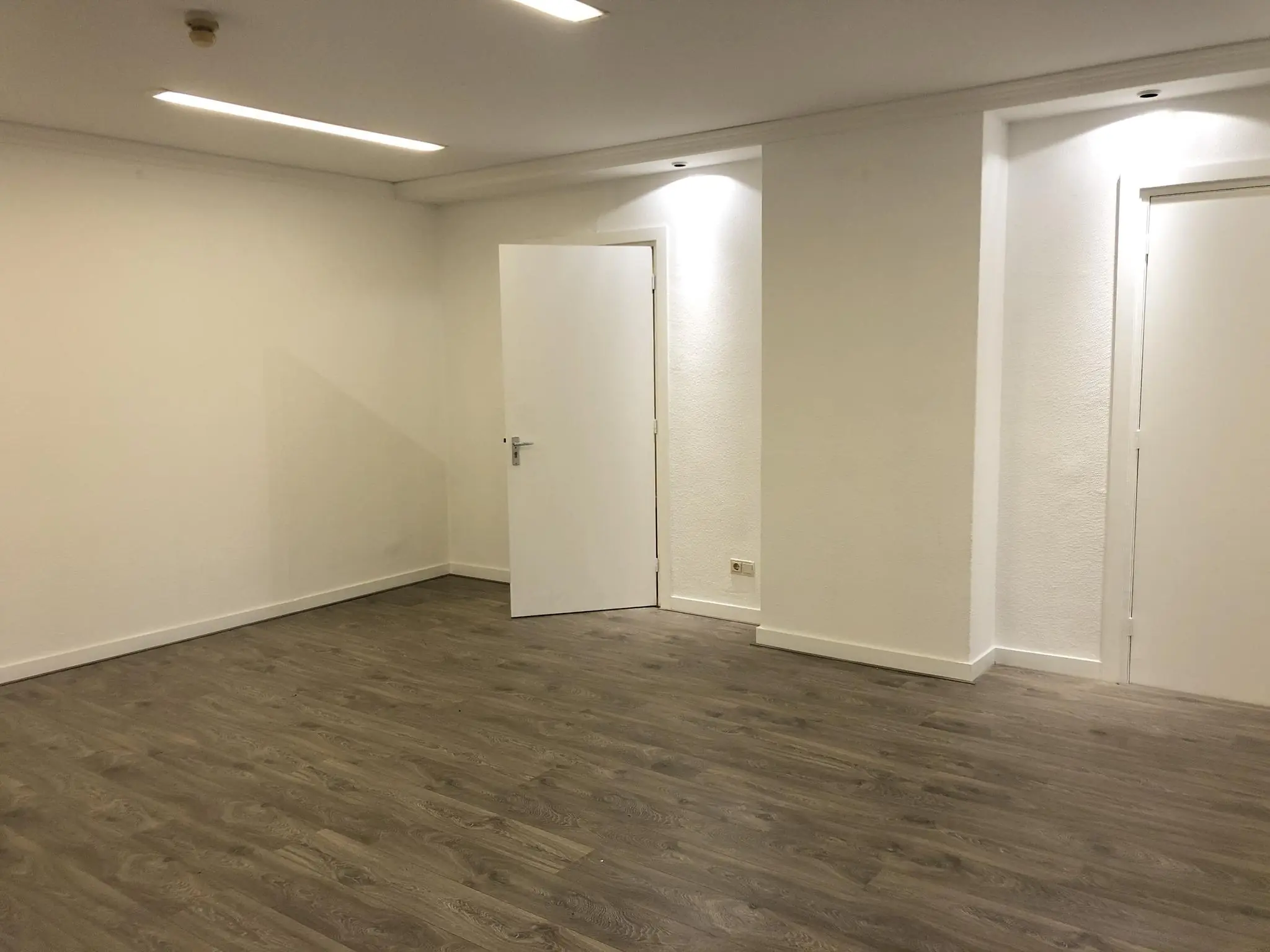 Lege kamer aan de Amersfoortsestraat met witte muren, houten vloer en twee witte deuren.
