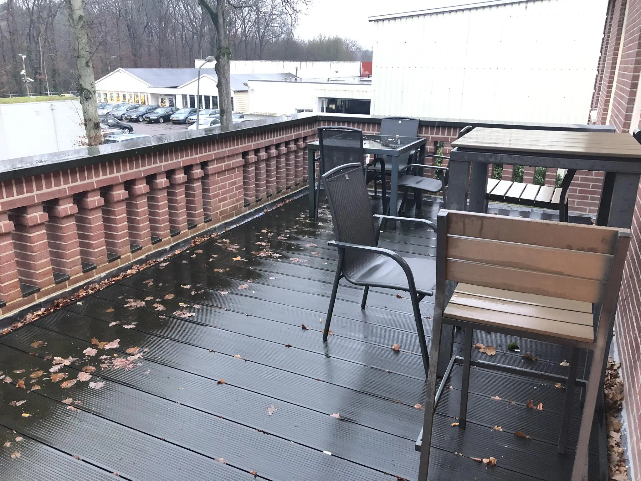 Buitenbalkon aan de Amersfoortsestraat met nat terras, herfstbladeren en zwarte terrasstoelen en -tafels.
