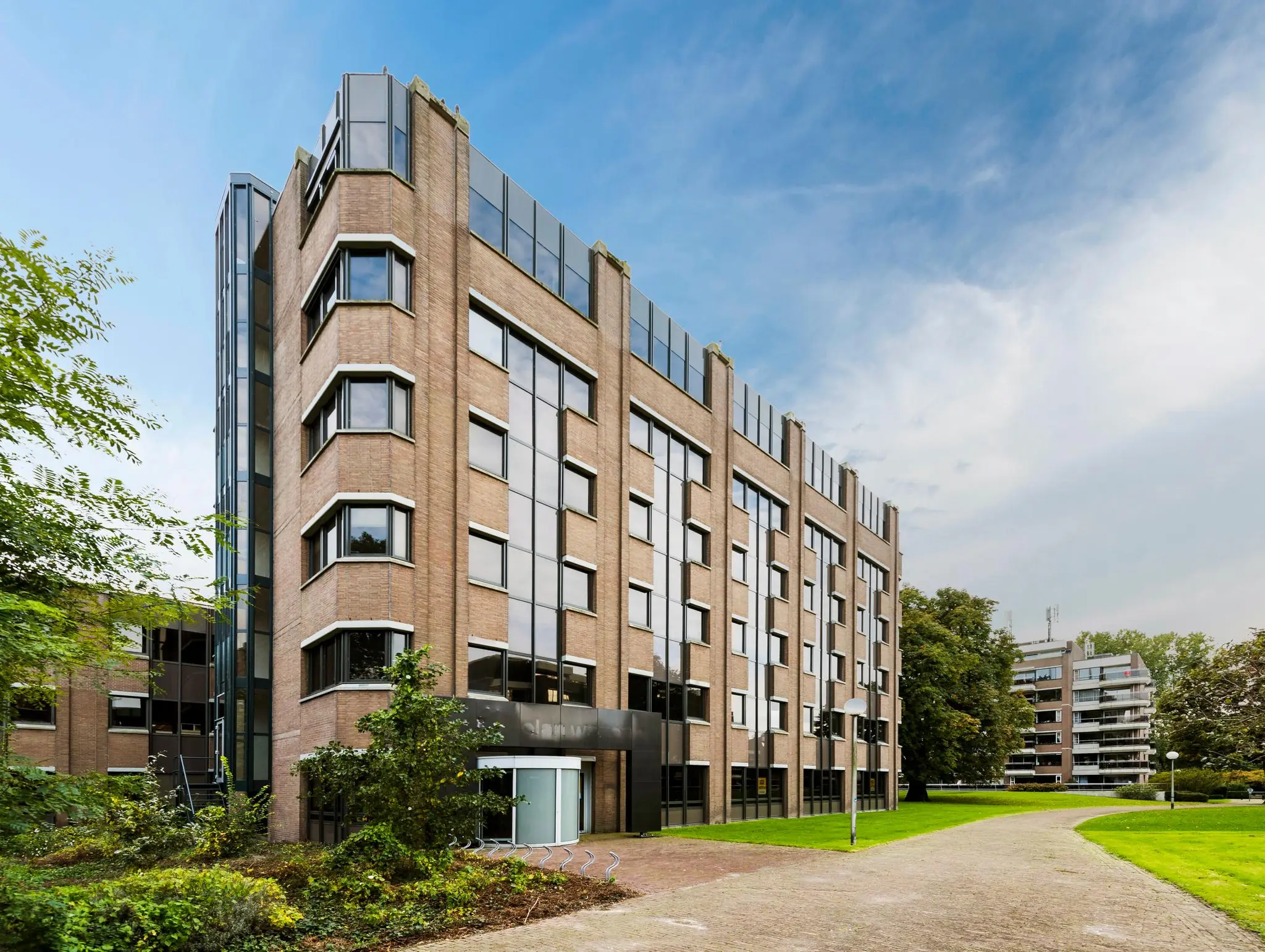 Zakelijk kantoorgebouw aan de Meesterlottelaan met gevel van baksteen en grote ramen, gelegen aan een groen wandelpad.
