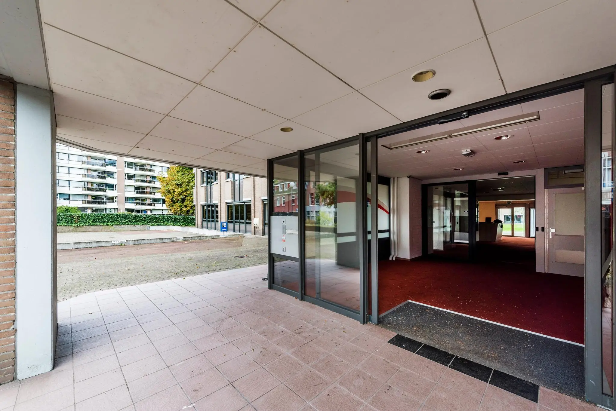 Ingang van een kantoorpand aan de Meesterlottelaan met glazen schuifdeuren en rode vloerbedekking binnen.