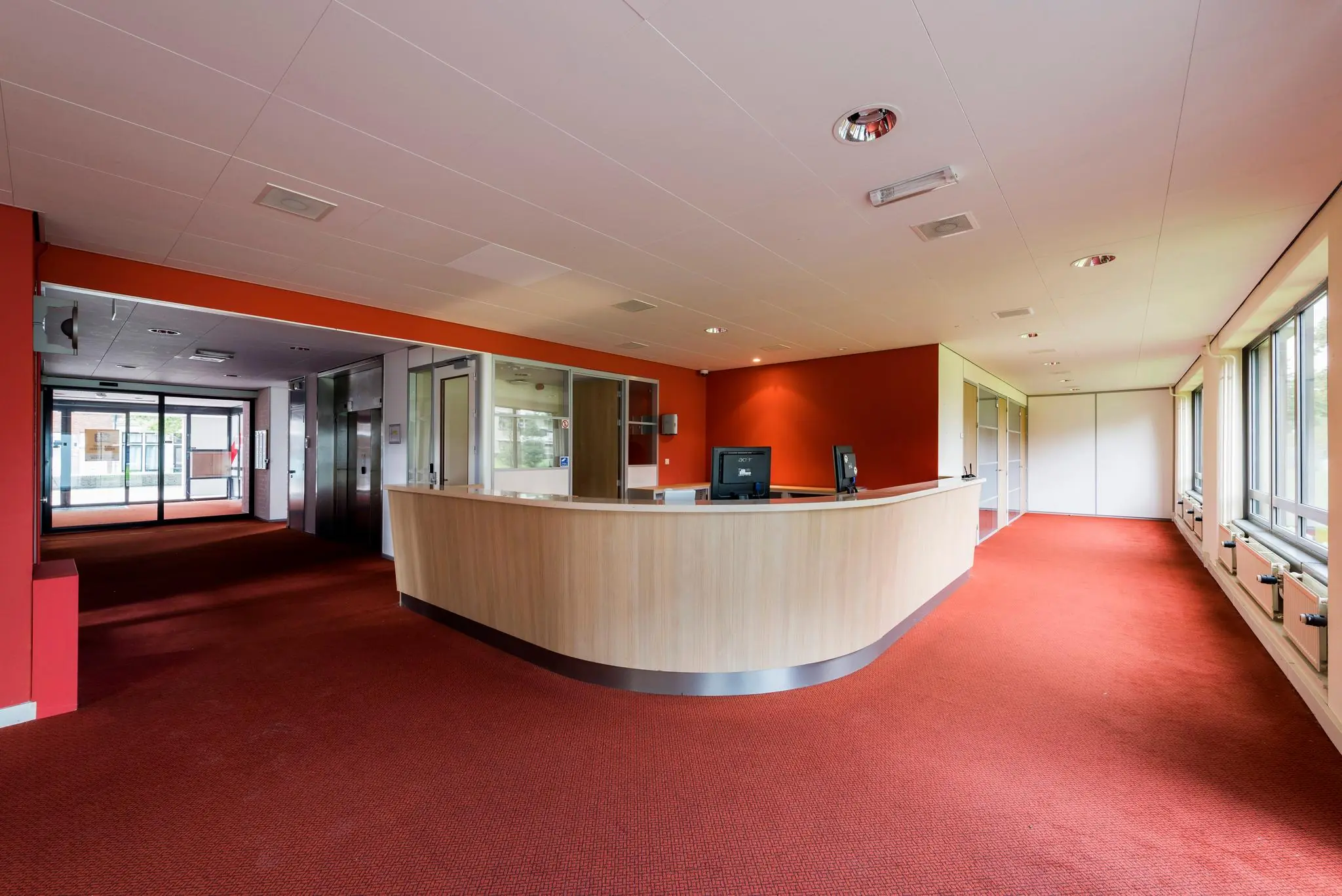 Receptiebalie in een modern kantoorinterieur aan de Meesterlottelaan met rood tapijt en glazen wanden.