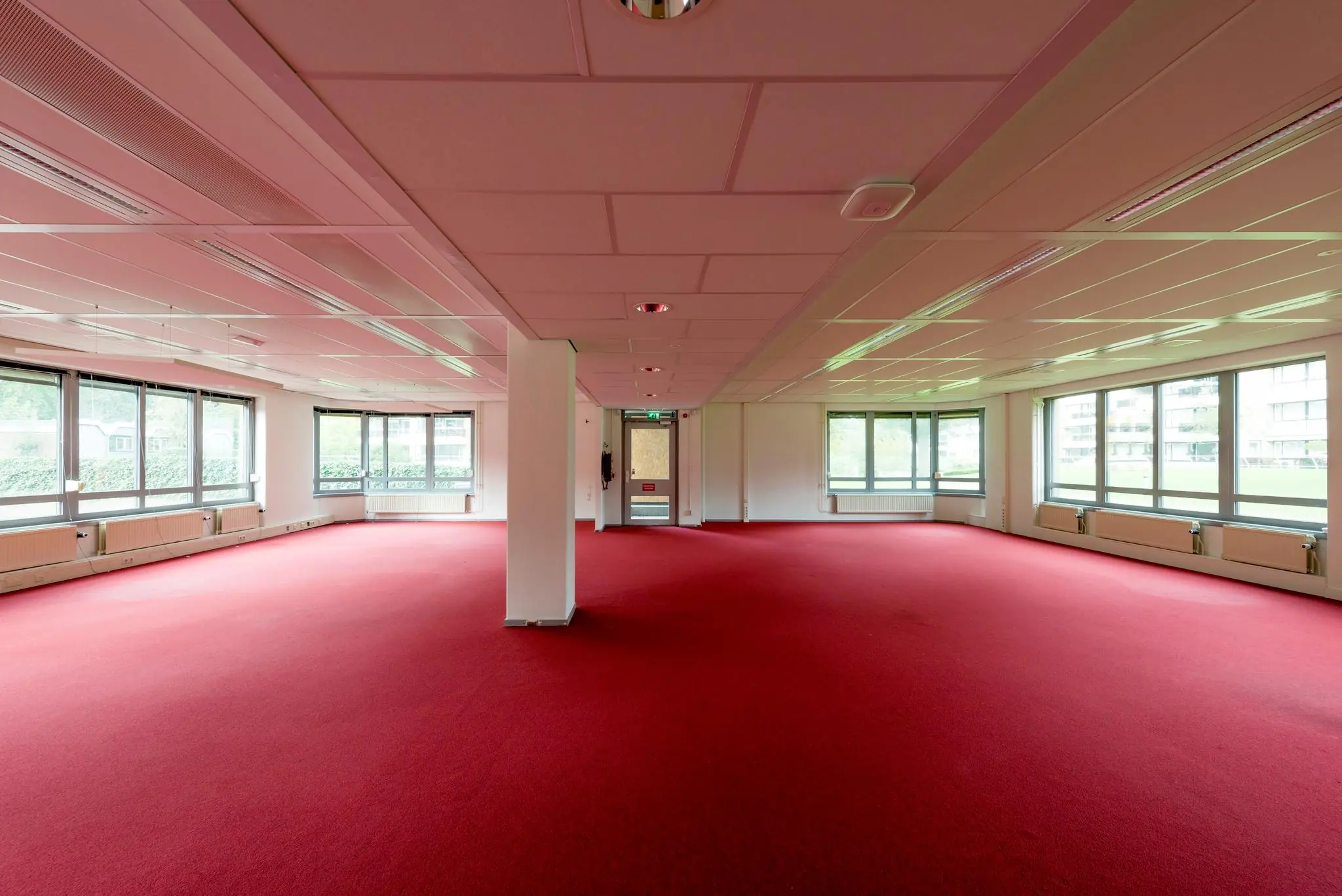 Lege kantoorruimte aan de Meesterlottelaan met rode vloerbedekking en grote ramen rondom.