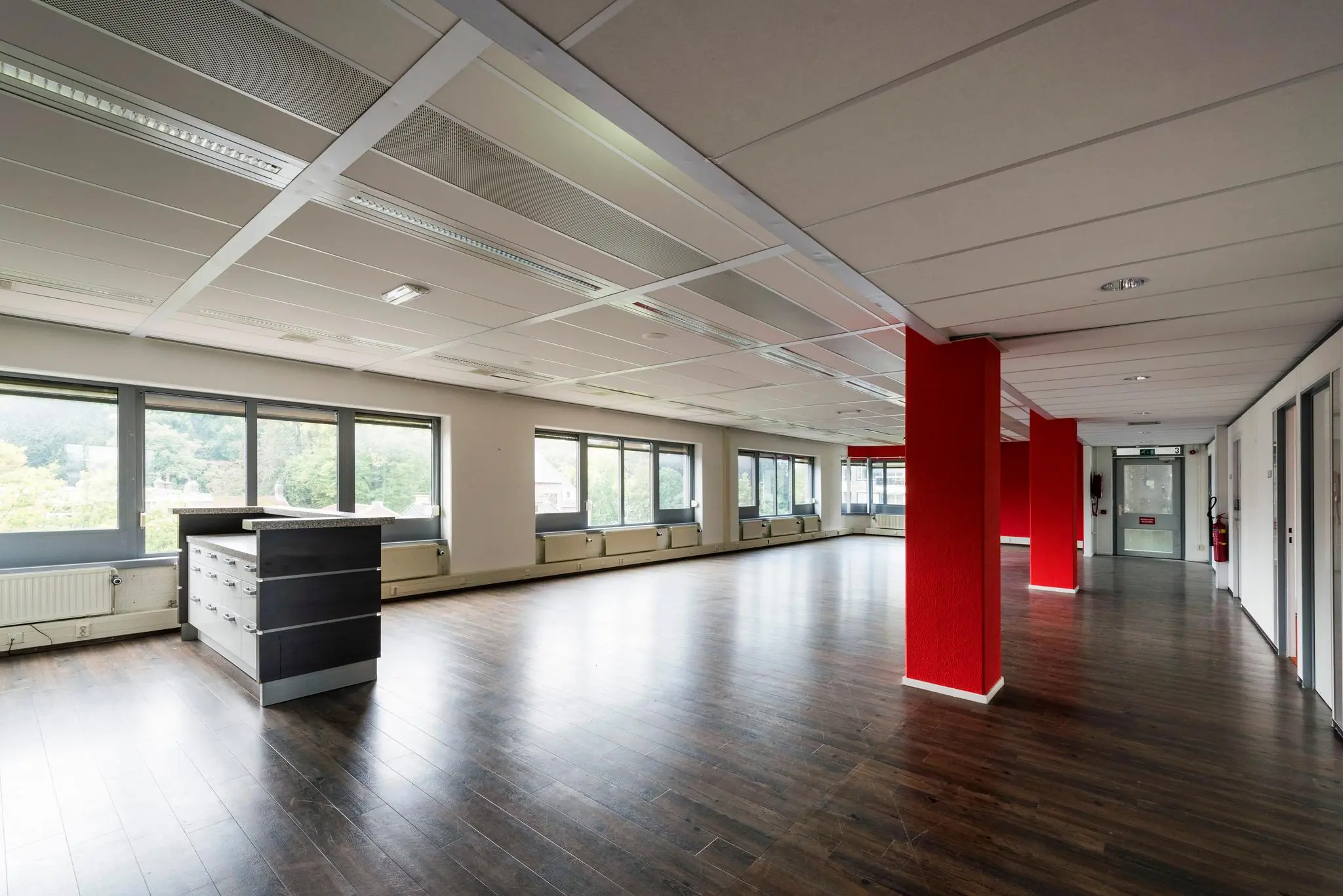 Ruime, lege kantoorruimte aan de Meesterlottelaan met grote ramen, donker laminaat en rode accenten.