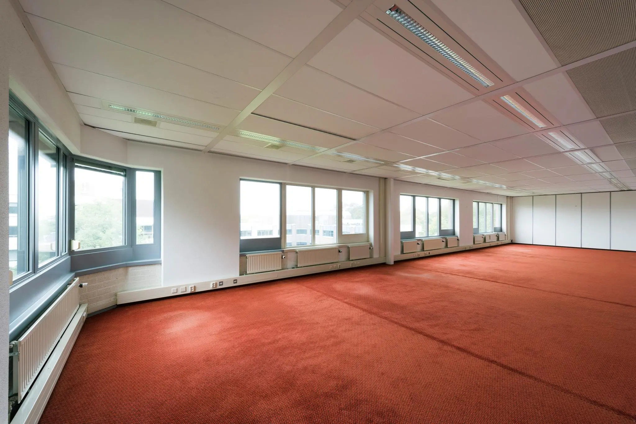 Ruime, leegstaande kantoorruimte aan de Meesterlottelaan met rode tapijtvloer en grote ramen.