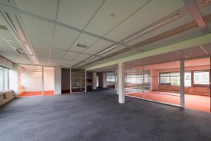 Leeg kantoorpand aan de Meesterlottelaan met glazen scheidingswanden en roodtapijt in aparte kantoorruimtes.