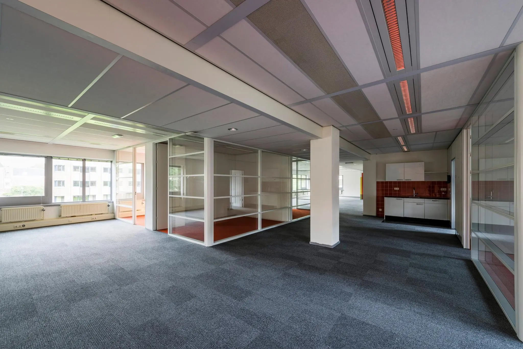 Moderne, lege kantoorruimte aan de Meesterlottelaan met glazen scheidingswanden, grijs tapijt en een kitchenette.