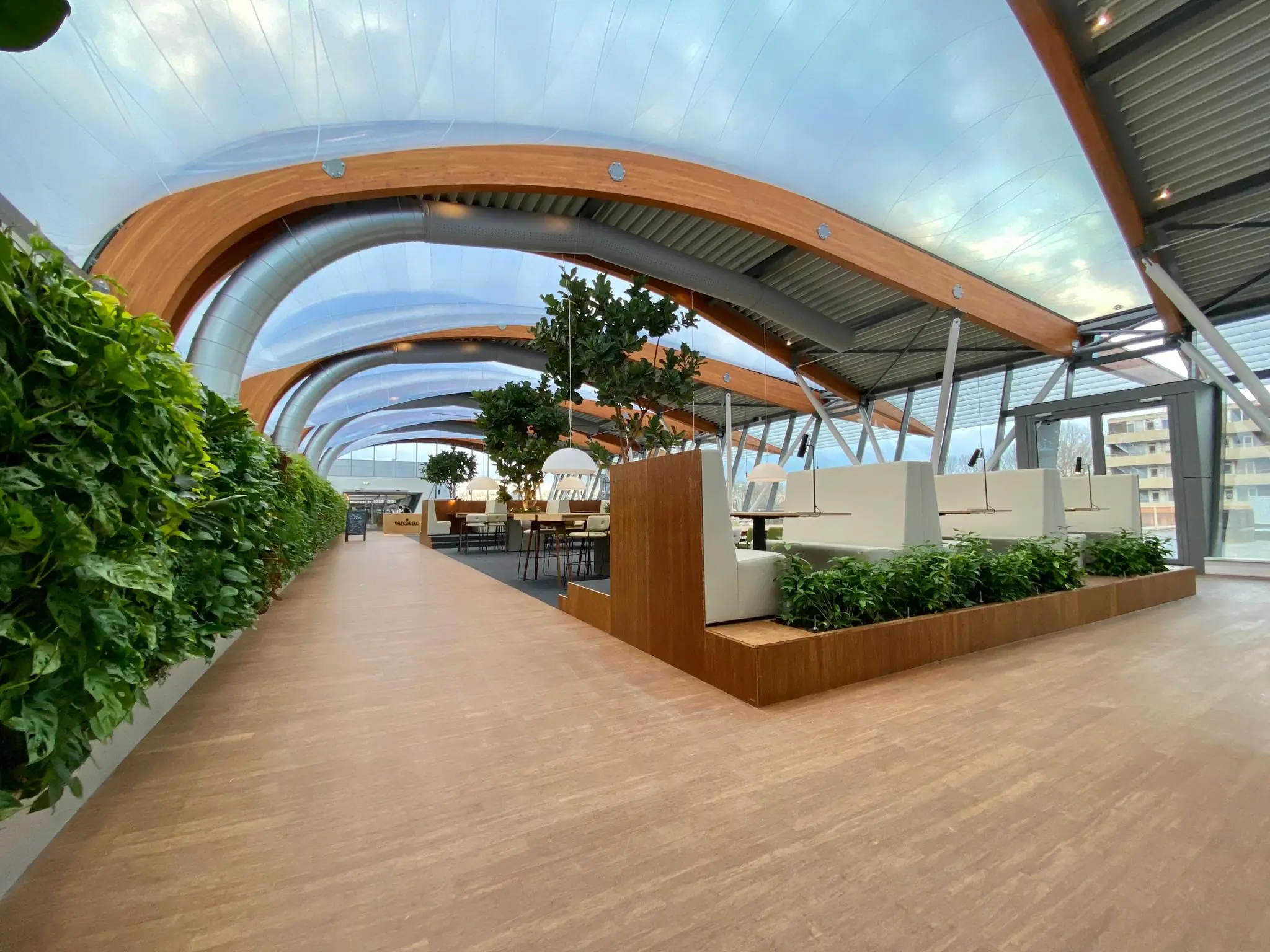 Moderne, lichte kantoorruimte in Bisonspoor met houten boogconstructie, plantenwanden en open werkplekken.