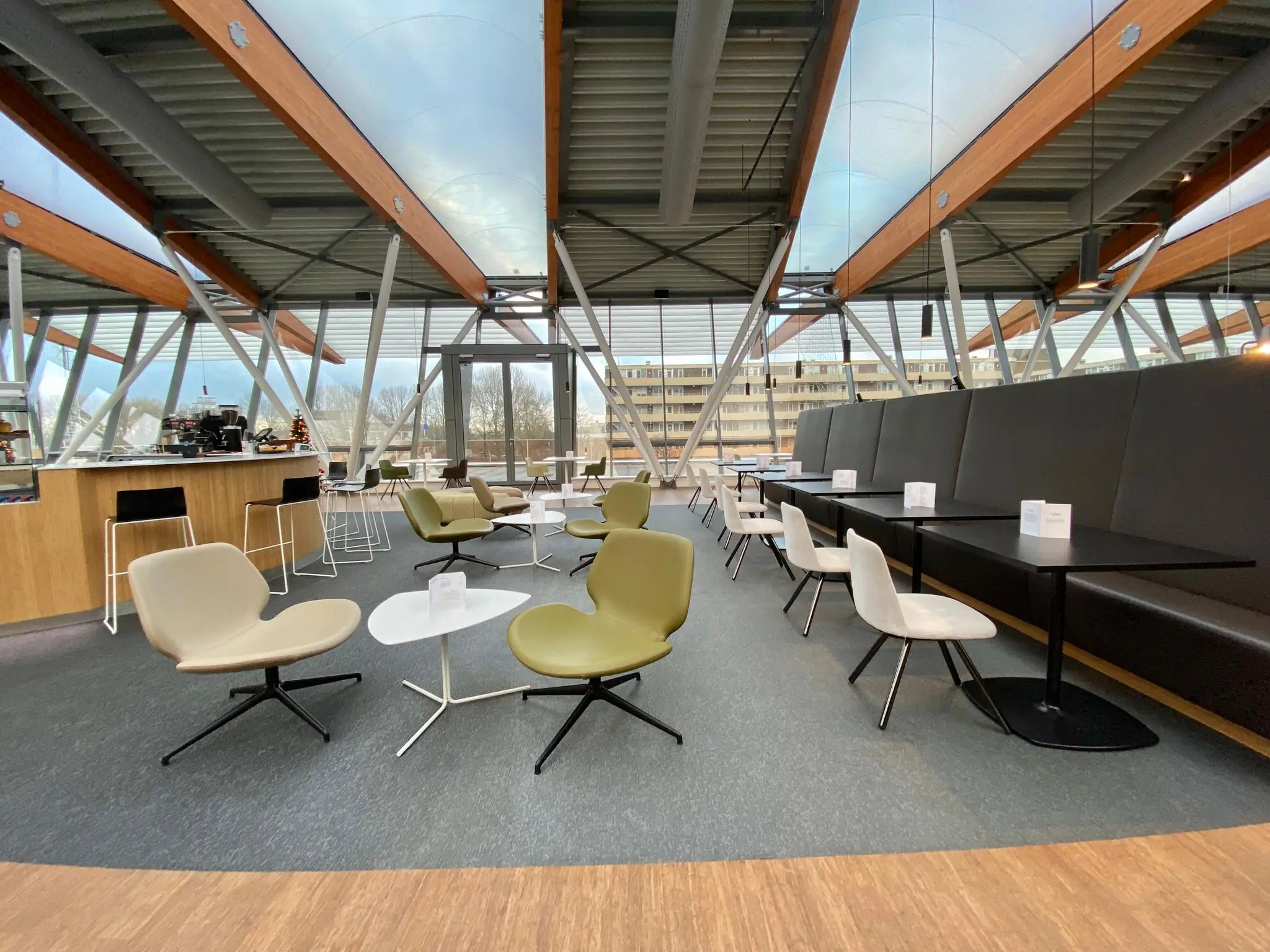 Moderne zitruimte in het Bisonspoor-gebouw met designstoelen, een bar en grote ramen die uitzicht bieden op omliggende gebouwen.